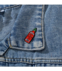 Macro shot of chili sauce bottle enamel pin with You're Hot text on denim jacket
