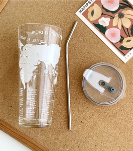 Close-up of glass tumbler with world map pattern, plastic lid and metal straw