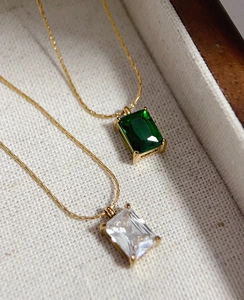 Macro view of emerald green and white square zircon pendants on gold plated chains