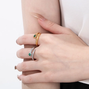 Detail of gold and silver snake rings with green gemstone eyes on female hand