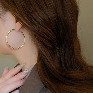 Close-up of a model wearing large minimalist golden hoop earrings with polished metal finish