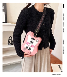 Detail of pink guitar-shaped crossbody bag featuring star, cross and wing decorations