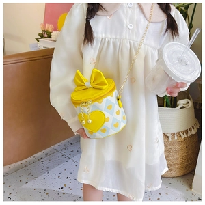 Detail of a yellow plaid children's bucket bag featuring a large bow and heart charm