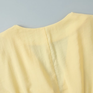 Close-up of the textured pale yellow fabric and seam detail on a V-neck lantern sleeve dress