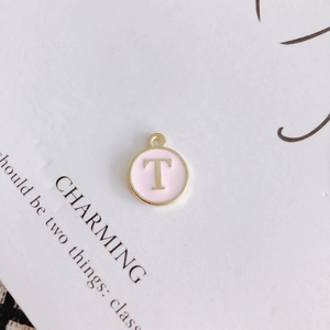 Detail of round gold-rimmed pink enamel charm featuring the letter T for DIY jewelry