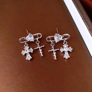 Detail of silver safety pin earrings with heart cubic zirconia and cross pendants