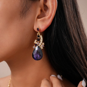 Close-up of teardrop purple crystal earring with gold setting worn on a model's ear