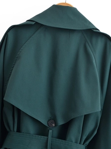 Detail view of the deep green trench coat back storm flap and decorative button
