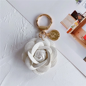 Close-up of white leather camellia keychain with a gold coin pendant and spring ring