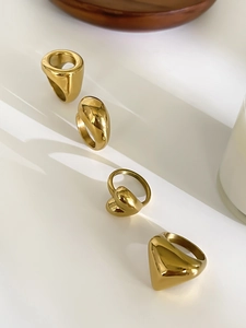 Macro view of four polished gold geometric rings on a white tiered minimalist display