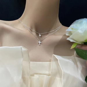 Detail shot of a silver layered necklace featuring a mini cross and teardrop stone pendant