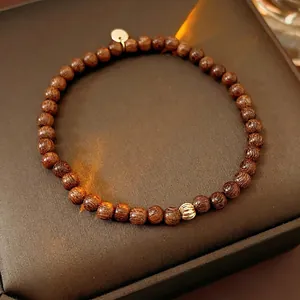Minimalist agarwood beaded bracelet with a gold charm and textured bead on a leather stand