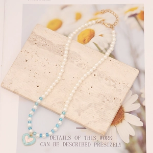 Detail of pearl necklace with blue beads and a colorful enamel heart pendant