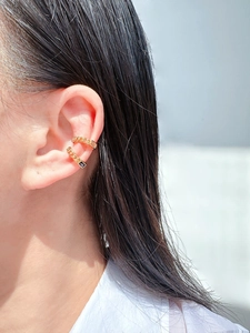 Detailed macro view of gold chain ear cuff featuring rectangular green and blue zircons