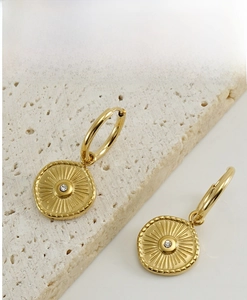 Detailed view of gold compass earrings with crystal on beige travertine stone