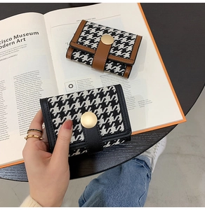 Detailed view of houndstooth wallet with leather trim and gold snap closure on a magazine