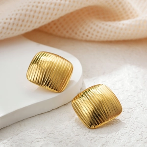 Close-up of golden square stud earrings with vertical striped texture and polished finish