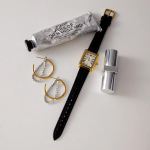 Flat lay of gold rectangular watch with black leather strap and sparkling hoop earrings