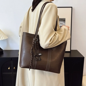 Brown leather tote bag with contrast stitching and cat charm shown on model