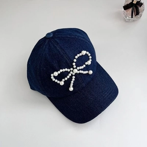 Detail of denim baseball cap with white pearl bow decoration on deep blue fabric