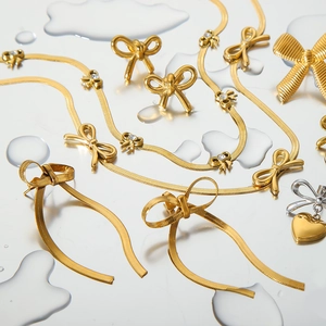 Detail of 18k gold plated bow earrings and heart necklace on water droplet surface