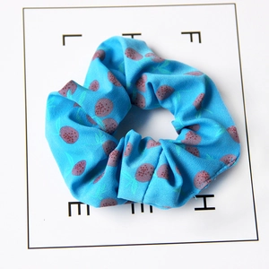 Detailed view of a light blue strawberry print fabric scrunchie on a white life card