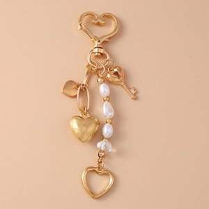 Detail of golden heart-shaped keychain with pearls and star pendants on beige background