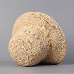 Détail d'un chapeau de paille beige tissé main avec texture ajourée et nœud décoratif