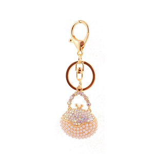 Golden handbag keychain pendant with white pearls and sparkling rhinestones on white background