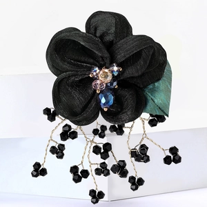 Detail of a black lace organza flower brooch with iridescent beads and golden tassels