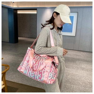 Pink travel bag with letter patterns shown on a model in a modern indoor setting