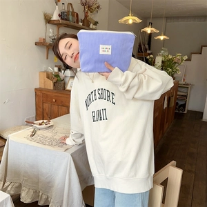 Close-up of purple corduroy cosmetic bag held by a model in a cozy cafe setting