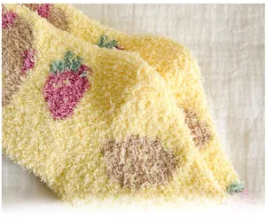 Close-up of soft yellow coral fleece socks featuring cute embroidered strawberry patterns