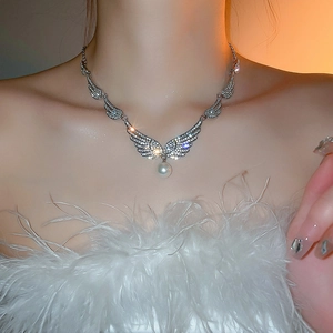 Close-up of wing necklace featuring shimmering zircon pave and a dangling pearl pendant