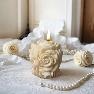 Candela profumata a colonna rosa color crema accesa su elegante tessuto con perle