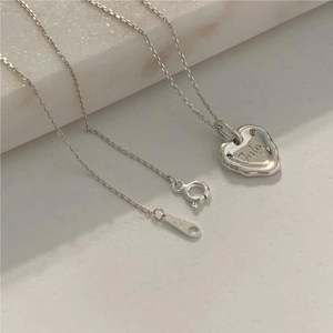 Detail of S925 sterling silver heart necklace with July engraving on marble surface