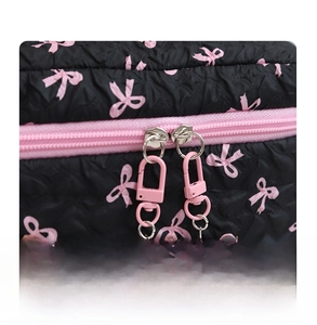 Detail of pink double zippers with pearl bow pendants on black quilted cosmetic bag