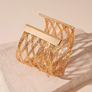 Detail of golden woven mesh cuff bracelet featuring hollow texture and polished metal edges