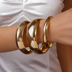 Detailed view of wide polished gold metal bangles set on a model's wrist with silk