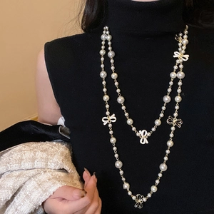 Detail of elegant layered pearl necklace with a white bow pendant on black sweater