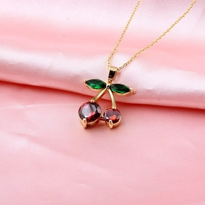 Elegant gold cherry pendant necklace with red and green crystals on pink silk fabric