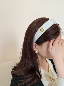 Primo piano dettagliato del cerchietto in tweed azzurro con logo in metallo dorato su modella