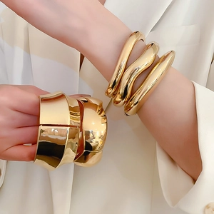 Polished gold wavy stackable bangles and wide geometric bracelets worn by female model