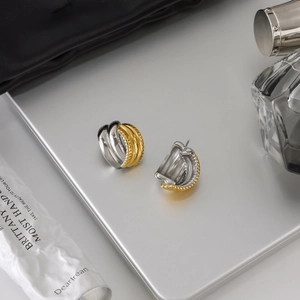 Close-up of dual-tone 18K gold and silver twisted C-hoop earrings on metal surface