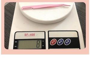 Pink stainless steel lash tweezer with comb showing light 8g weight on digital scale