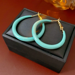 Gros plan de grandes créoles en émail turquoise avec fermoirs dorés sur un écrin à bijoux