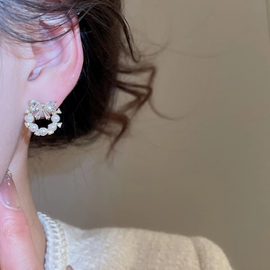 Detail of bow-knot pearl wreath earring with gold base and zircon accents on model
