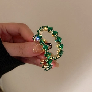 Détail de cristaux carrés verts sertis dans une boucle d'oreille dorée avec reflet étoilé