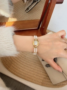 Elegant gold watch with a pearl bead bracelet and white dial worn on a female wrist