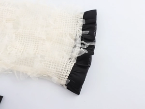 Détail de manche en mesh blanc avec bords effilochés et poignets à volants noirs